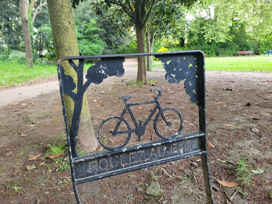 Panneau "roulez au pas" en métal, formant une silhouette de vélo et d'arbres découpés.