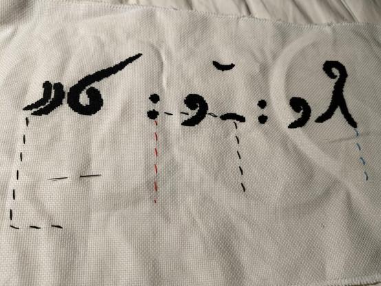 An unfinished cross stitch of a phrase in the fictional language from the game Heaven's Vault. The first row of symbols is done, and there are four columns of guiding stitches to make sure the second row goes in the right place.