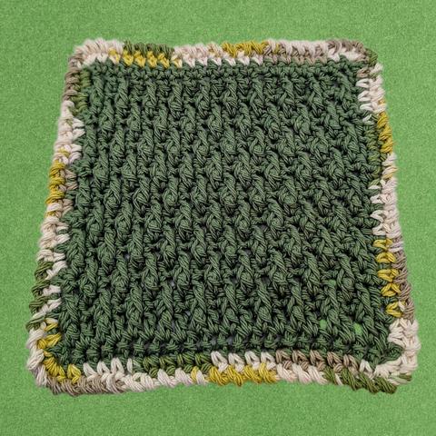 A crocheted 100% cotton dishcloth made with alpine stitch and an imitation crab stitch border. The main part is army green, and the border is multicolored with cream, tan, yellow green, and army green.