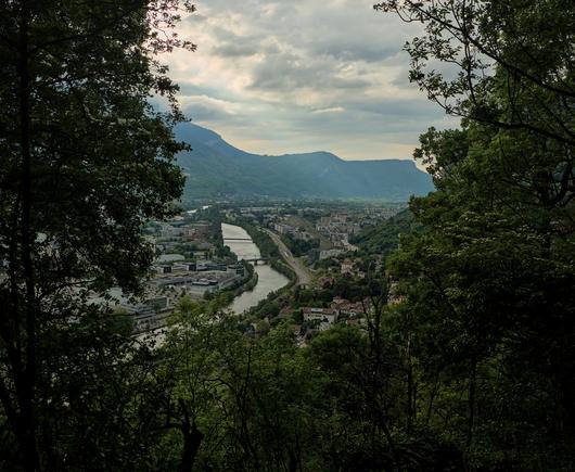 Vue à travers les arbres où on peut distinguer l'isère ainsi que le vercors en arrière-plan