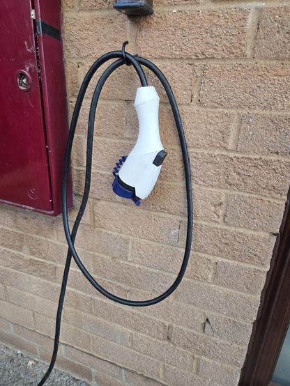 An electric vehicle charging plug hung from a black cup hook on a brick wall