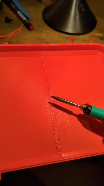An orange 3d printed box lid and a pinecil solder iron is visible. There is a ridged weld pattern on the lid.