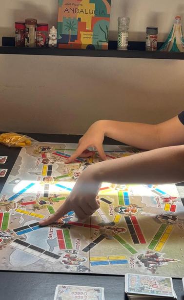 Two kids playing the board game Ticket to Ride, as the dying sun streams in from the window.