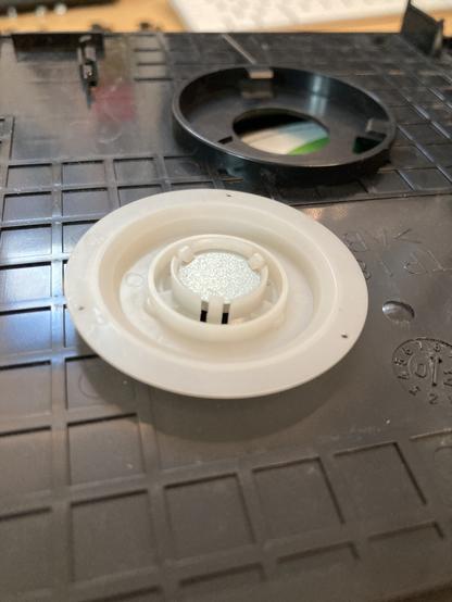 The tray spindle is a plastic disc. It is shown in its original design, removed from the tray showing the flimsy magnet inside.
