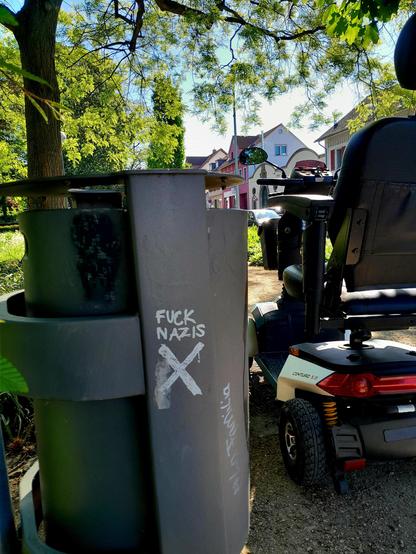 The scoot-chair is parked next to a trash can emblazoned with FUCK NAZIS, and the Shitter logo, which is a sans-serif swastika.