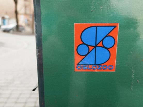 A rectangle sticker with an red-orange background featuring a blue geometric design with intersecting circles and lines forming an S figure. The text 'OSLOZOO' is written in blue letters at the bottom.