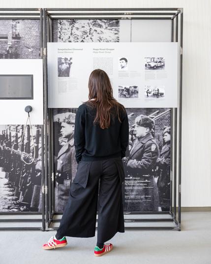 Eine Frau guckt sich die Ausstellung an. Sie trägt dunkle Kleidung und steht mit dem Rücken zur Kamera.