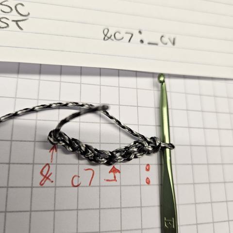 an crochet hook finishing the 7th stitch of a chain. there is writing below the chain to depict the instructions: &  c7 :