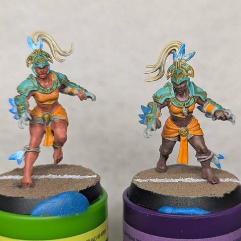 Two painted plastic miniatures of dark skinned women with white hair dressed for Blood Bowl.  They are wearing helmets, shoulderpads, and armguards that have short claws extending past their knuckles.  Their armor is aqua with dull gold details, and their uniforms are orange.  They have light blue feather decorations as well.