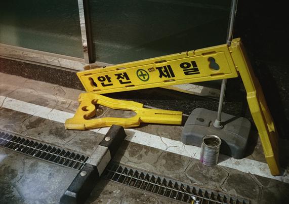노란색 '안전 제일' 차단펜스. 다리 한 쪽이 부러저 쓰러진 채 방치되어 있다.