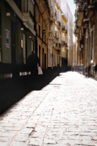 A man on the left is walking up a narrow street with colorful houses on both sides.