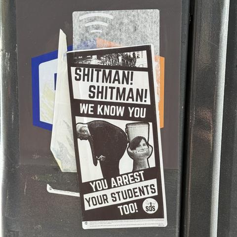 A sticker on the side of a traffic signal box on a lamp post reading “Shitman! Shitman! We know you — you arrest your students too!” with a cutout of Donald Trump taking a dump on a toilet with Claire Shipman’s (acting president of Columbia University) head in the toilet.