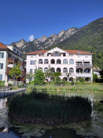 Foto. Ein weisses Gebäude mit Teich in Berglandschaft.