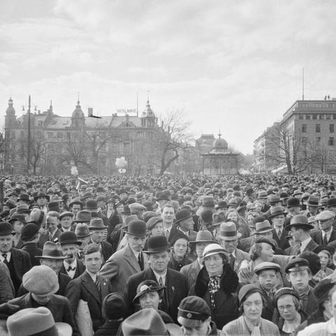 A large gathering of people on International Worker's Day 1936. In the background, a large hotel.