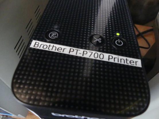 A 0.25" wide label printed in black ink on white tape affixed to the top of a Brother label printer that reads "Brother PT-P700 Printer".