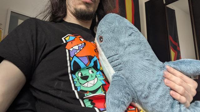 Me wearing my pawloroid shirt holding my blahaj against my chest