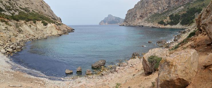 A panoramic photo of a bay surrounded by rocky hills. The sky is hazy.