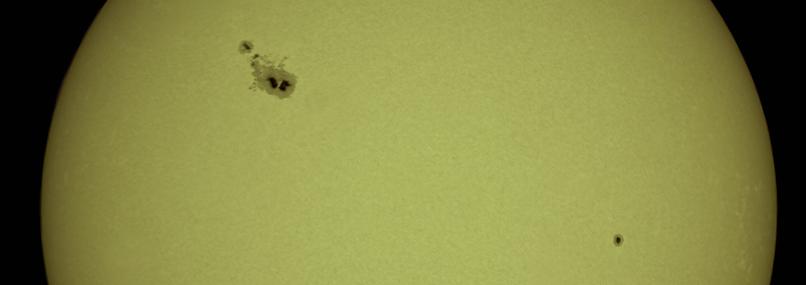 A close-up of the Sun showing a large group of sunspots in the upper left area and a single smaller sunspot in the lower right.