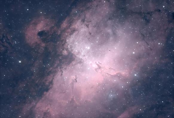 A large bright star forming nebula. A cluster of bright stars sits at the center, causing all the hydrogen gas around them to glow pink. Tiny dark cocoons are silhouetted in front. Finger-shaped pillars of gas and dust reach from the bottom and right side towards the center - the "pillars of creation".