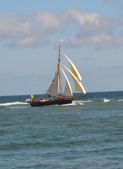 Einmastiges Segelschiff mit schwarzem Rumpf unter vollen Segeln, türkisfarbenen See.