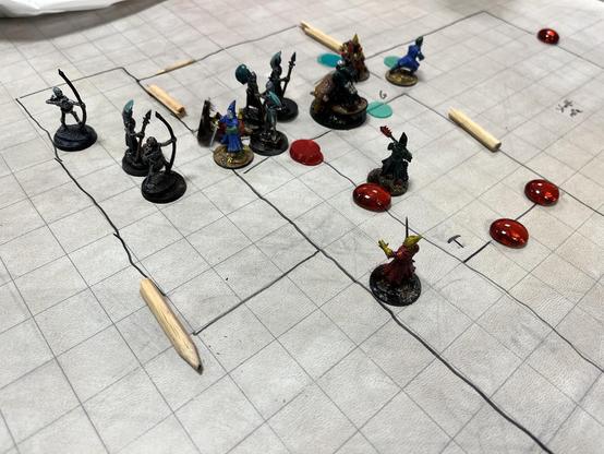 Einige Minis auf einer Battlemap auf der einige Räume eingezeichnet sind. Kaputte Bleistifte dienen als Türen. Es sind einige Marker zu sehen. Die Minis sind mittelalterliche Kämpfer. Sie werden von Skeletten angegriffen.
