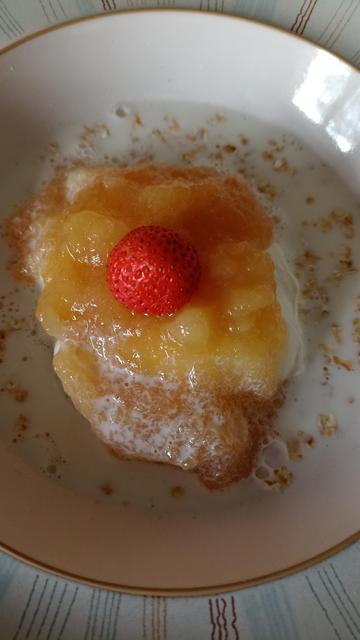 A small strawberry on yellow apple puree in a bowl of milky cereal