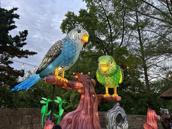 2 lit parrots, one green and one blue, perched on a lit tree.