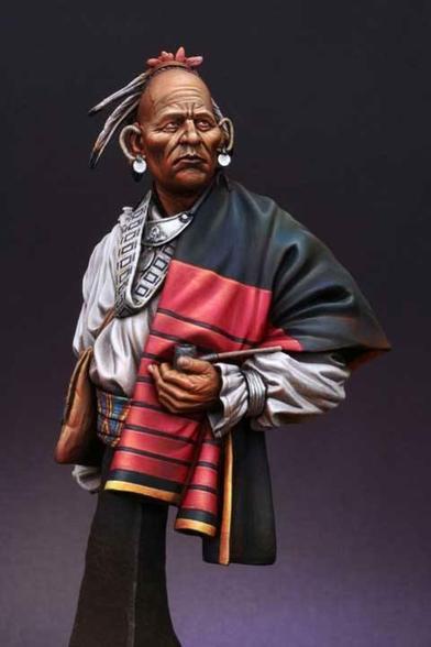 This image is an exquisitely painted miniature sculpture of a Native American elder, radiating dignity, wisdom, and cultural richness. The figure is sculpted with striking attention to detail. The elder’s face is deeply lined, each wrinkle conveying a story of experience and resilience. His expression is one of quiet thoughtfulness, with furrowed brows and slightly pursed lips that hint at introspection. The skin tone is rendered with remarkable realism, capturing the subtle variations of age and outdoor life.