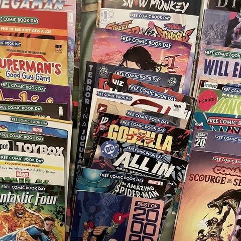 A collection of various comic books displayed together. The titles include "Superman's Good Guy Gang," "Fantastic Four," "Godzilla," "The Amazing Spider-Man," and several others, all labeled as part of "Free Comic Book Day."