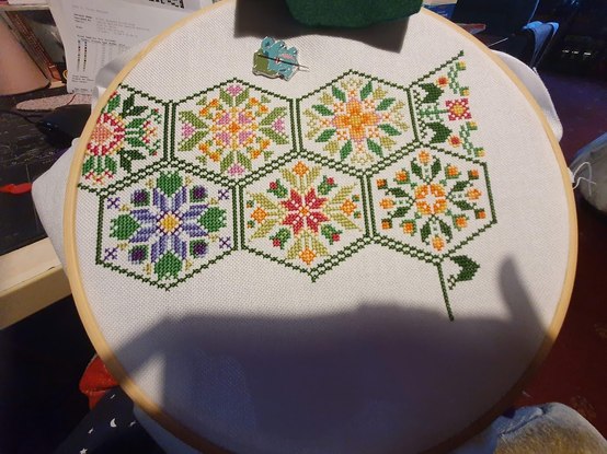 Another photo of the floral hexagon sal. There are now 2 rows of 3 green hexagons filled with brightly coloured flowers. There is one half hexagon that reaches the edge of the pattern.