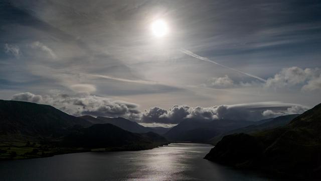 Sunshine over lake waters frames by mountains and cloud streaked sky