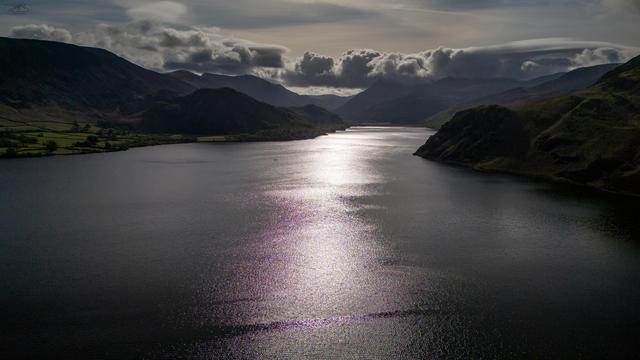 Sunshine over lake waters frames by mountains and cloud streaked sky