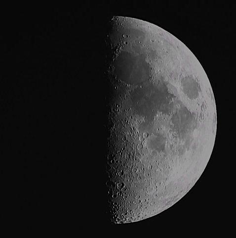 The Moon at first quarter phase on a dark background.
