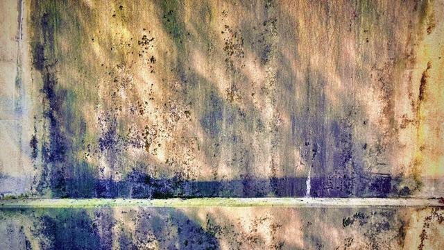 Bright orange and shaded blue light reflect on a beige stone wall from unseen rippling water below.