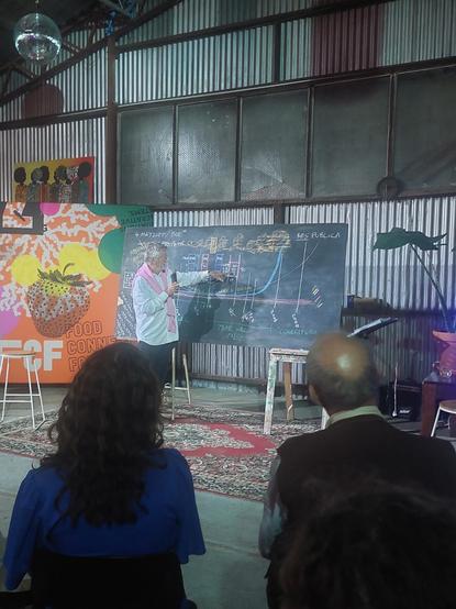 Christopher Budd presenting in front of a blackboard where he has drawn many diagrams.