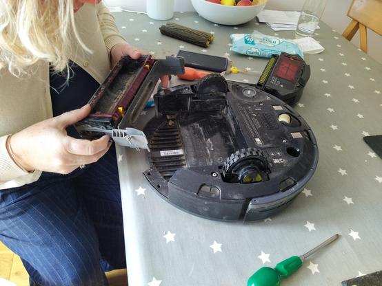 A robot hoover upside down on a table in bits and surrounded by hand tools.