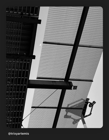 Outside of an airport looking up all you see is the side of a building a night flood light and the moon between the metal structures!