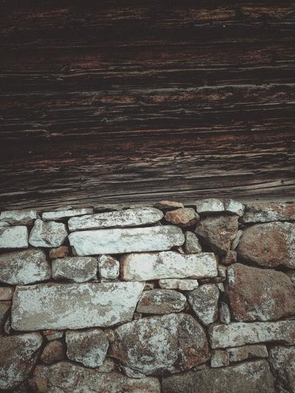 Part of a wall and the hut on top of it. Horizontal wooden beams on a partially painted dry stone wall.