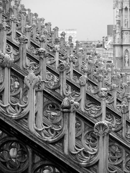 Black and white photo looking at a progression of flying buttresses on a cathedral. Each of the buttresses is topped with a series of elaborately carved stone finials.