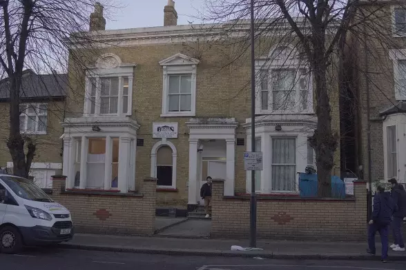 The image depicts a building, likely a residential structure, featuring a mix of brick and architectural elements. There are large windows and a prominent entrance. A sign is visible above the entrance, and there appears to be some activity outside, with people nearby and a vehicle parked on the street. The overall aesthetic seems to be typical of a suburban area.

Image Credits: Wikimedia / Jwslubbock / CC BY-SA 4.0
