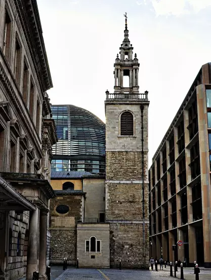 The image features a historic building with a tall clock tower, alongside modern architecture. The tower has a distinctive spire, and the older structure is made of stone. In the background, there's a modern glass dome structure, contrasting with the older style of the building. The scene is set in an urban environment, likely characterized by shops or offices nearby. The lighting suggests a daytime setting.

Image Credits: Wikimedia / It's No Game / CC BY 2.0