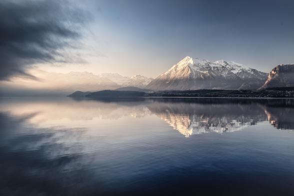 Thunersee mit Niesen, der sich auf der Wasseroberfläche spiegelt. Vom linken Rand greift Nebel ins Bild.