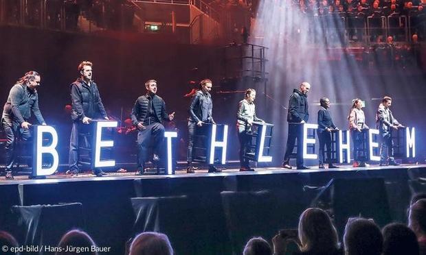 Menschen stehen auf einer Bühne und halten Buchstaben, die zusammen "Bethlehem" ergeben