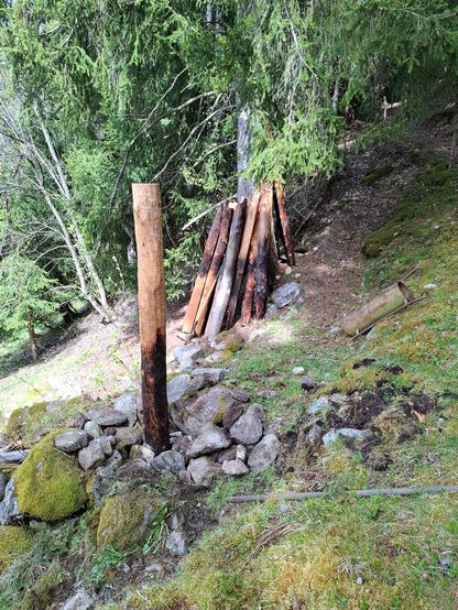 Round larch column wedged and fixed with stones. Burnt fence leaning on a big spruce tree in the background on a stony ground in the forest