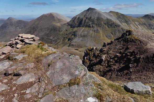 The small, almost disappointing summit cairn of Beinn Tarsuinn is backed by the boulder screes of the ridge from Sgùrr Bàn to Beinn a' Chlaidheimh in the distance.