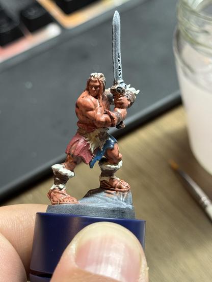 The HeroQuest Barbarian on a paint handle. The body is base colored with the hair and sword missing so far. It is shown from the front.