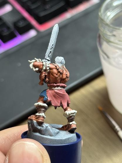 The HeroQuest Barbarian on a paint handle. The body is base colored with the hair and sword missing so far. It is shown from the back.
