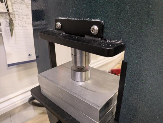 The blob of silver is lined up over a die, on the pressing plate of a hydraulic press.