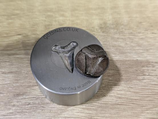 The blob of silver has been taken out of the die. It has taken some of the shape of the die (shark's tooth), but not filled it completely.