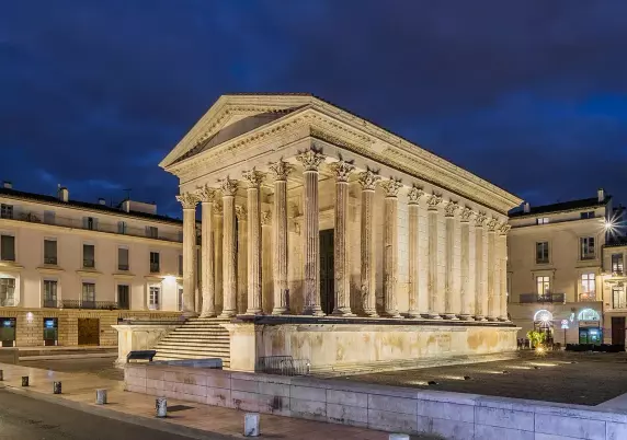 The image depicts a classical-style building with a portico supported by columns. This type of architecture typically features a rectangular shape and is often associated with temples or public buildings in ancient cultures. The structure appears to be well-lit against a night sky, highlighting its details. It is situated in a plaza or open area, surrounded by other buildings. This setting could suggest it is a significant historical or cultural site.

Image Credits: Wikimedia / Krzysztof Golik / CC BY-SA 4.0